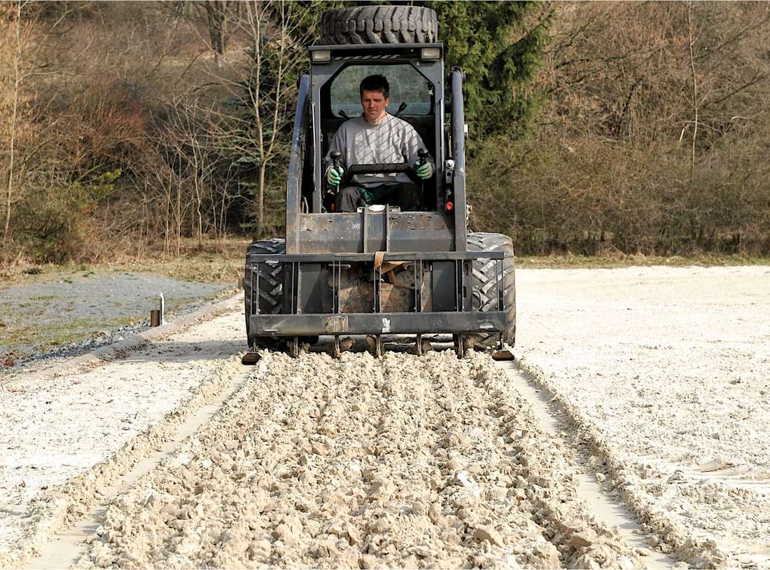Mann mit Maschine lockert den sandigen Boden eines Reitplatzes
