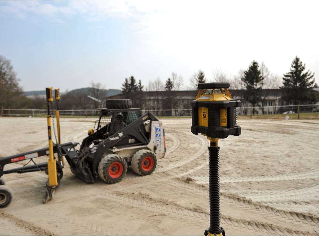 Planierungsgerät und Nivelliergerät stehen auf einem sandigen Reitplatz