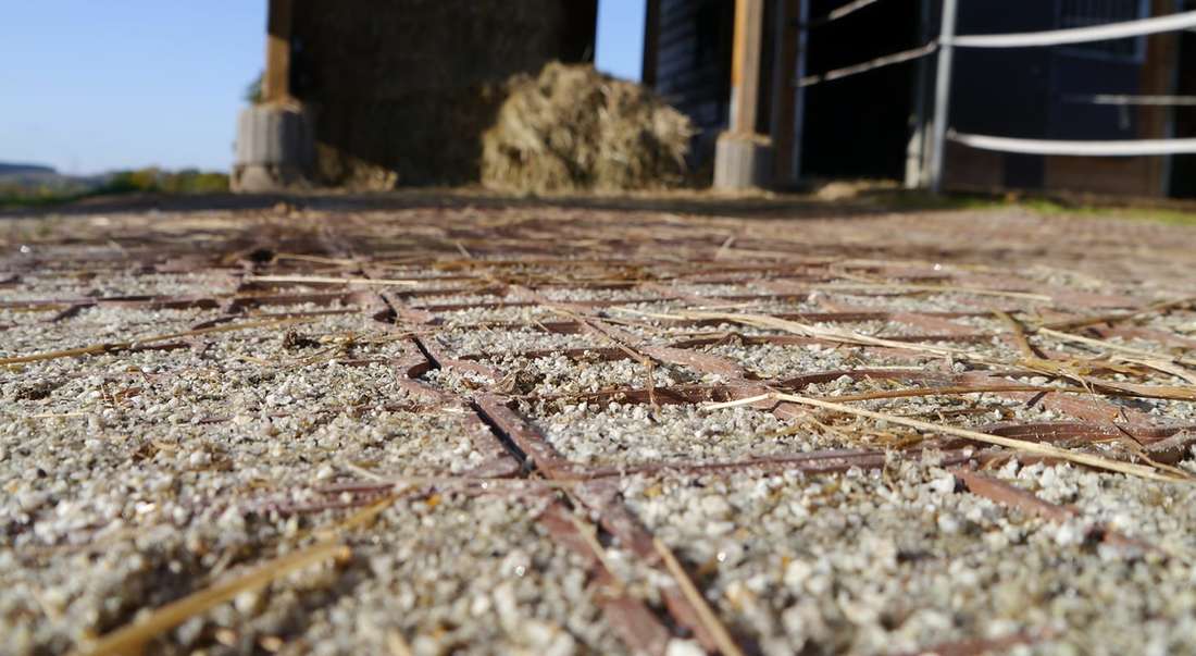 Nahaufnahme von terrakottafarbigen ECORASTER Bodengitter mit Stall im Hintergrund
