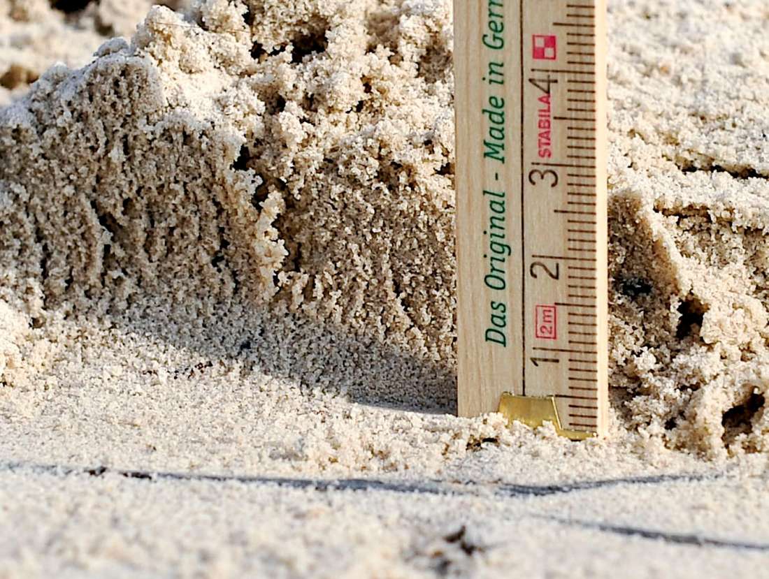 Nahaufnahme eines Zollstock vor einem Sandhaufen