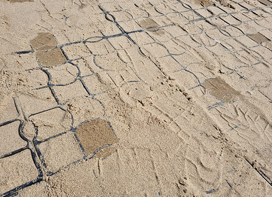Eine mit Sand befüllte ECORASTER Fläche mit dunklen Wasserflecken
