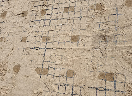 Draufsicht auf eine mit Sand befüllte ECORASTER Fläche mit einzelnen Wasserflecken